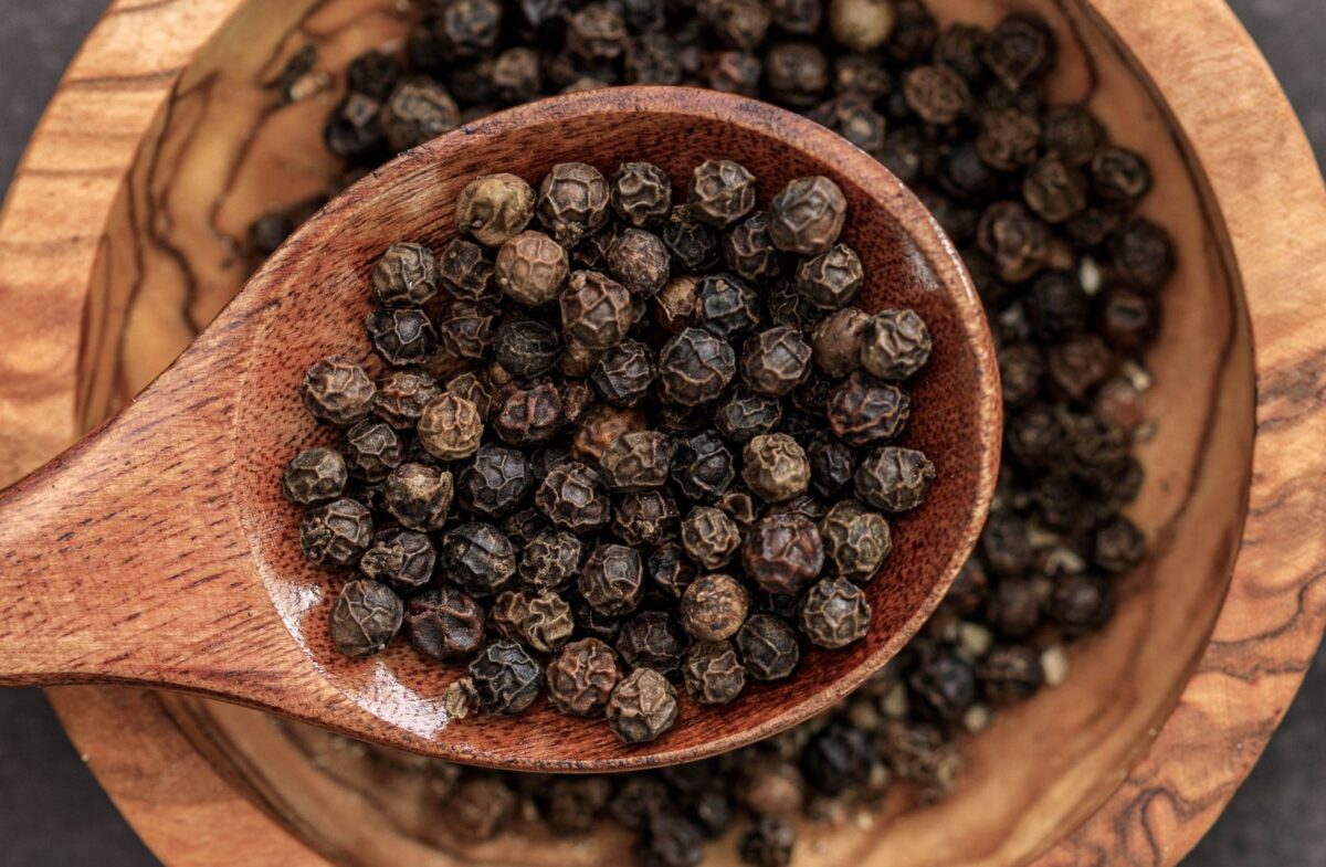 Black peppercorns in a wooden bowl and spoon, the source of piperine