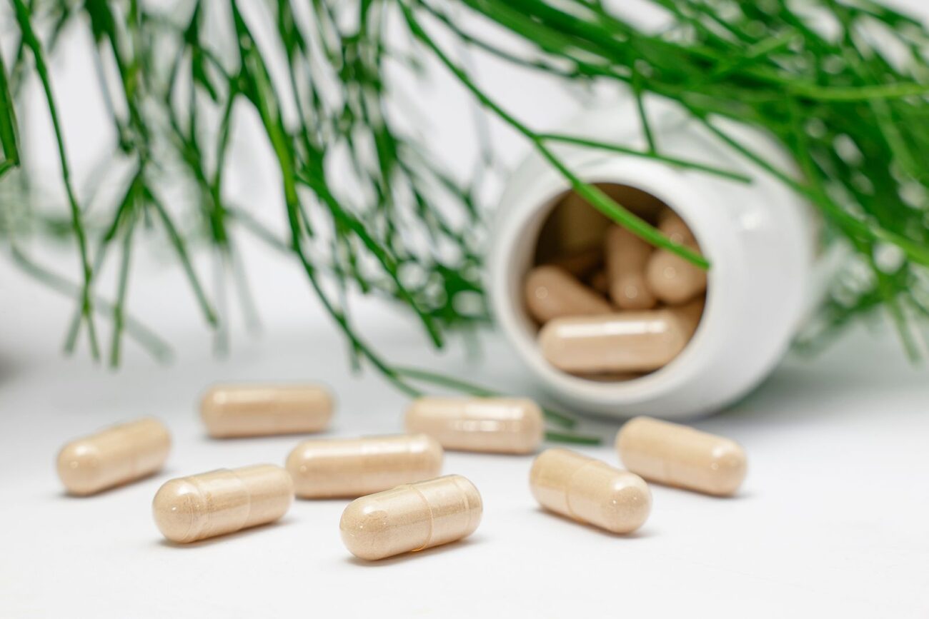 Plant-based supplement capsules spilling from a bottle beside green foliage