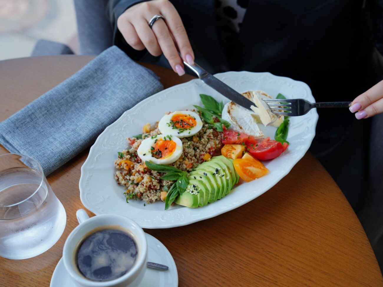 A plate of eggs, grains, avocado and vegetables being eaten at a table