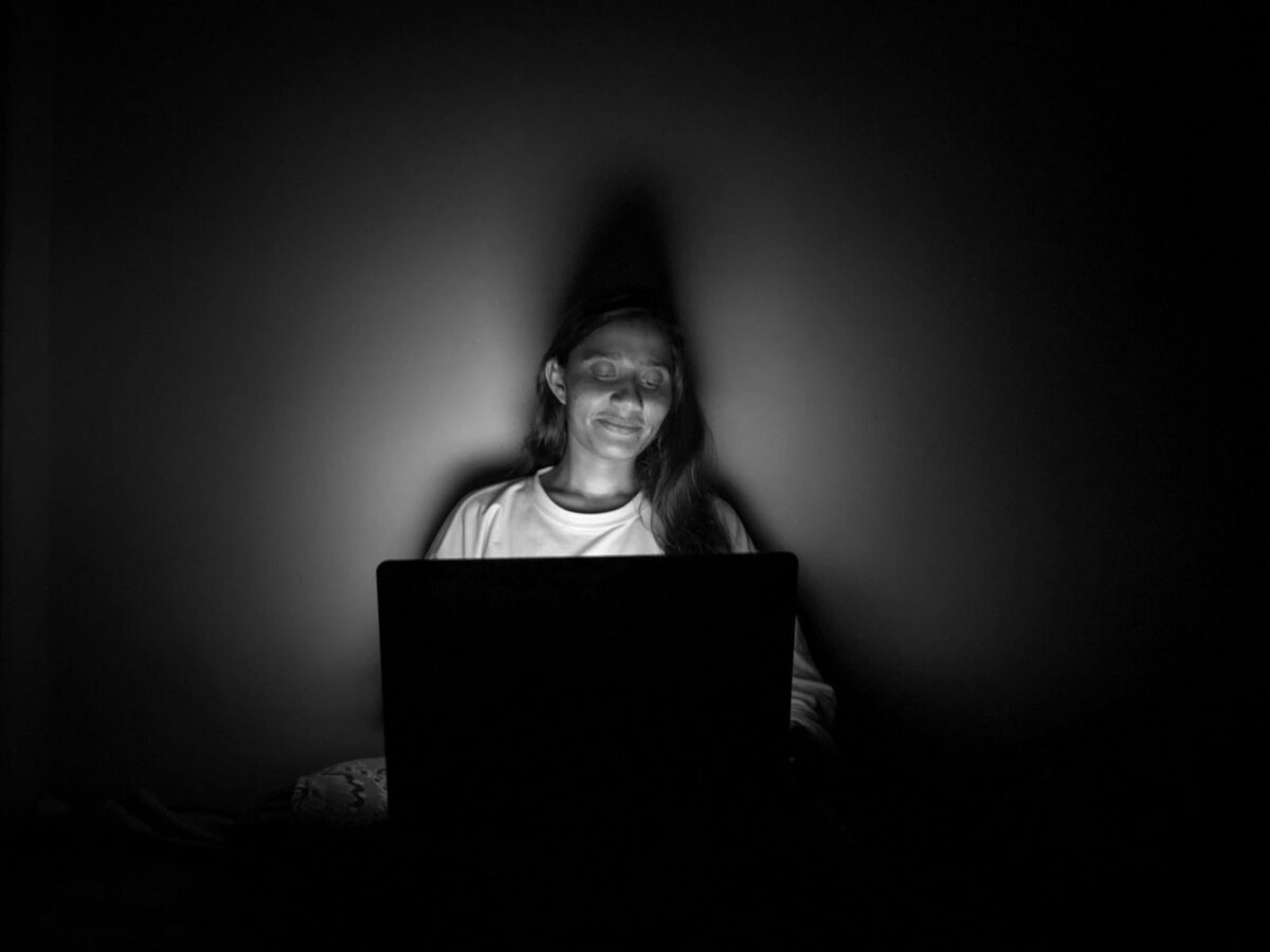 A person lit only by a laptop screen in a dark room