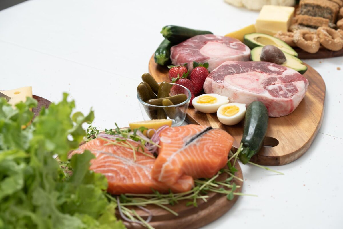 Salmon, lean meat, boiled egg, cheese and fresh vegetables arranged on a wooden board