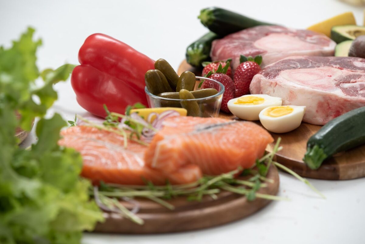 Salmon, red meat, boiled egg and fresh vegetables arranged on a wooden board