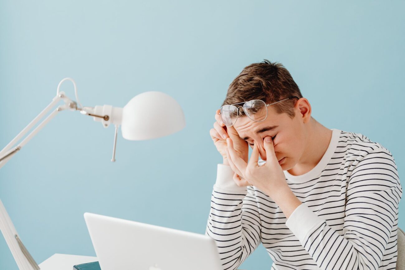 A tired person rubbing their eyes while sitting at a laptop
